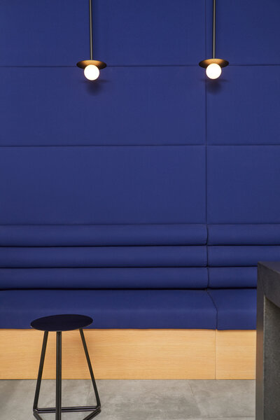 A plush, deep blue bench and wall and black stool lit by two small globe pendant lighting fixtures