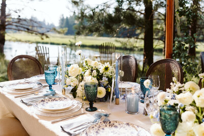 Outdoor wedding reception table styled with tapered candles and floral arrangements in a natural setting.