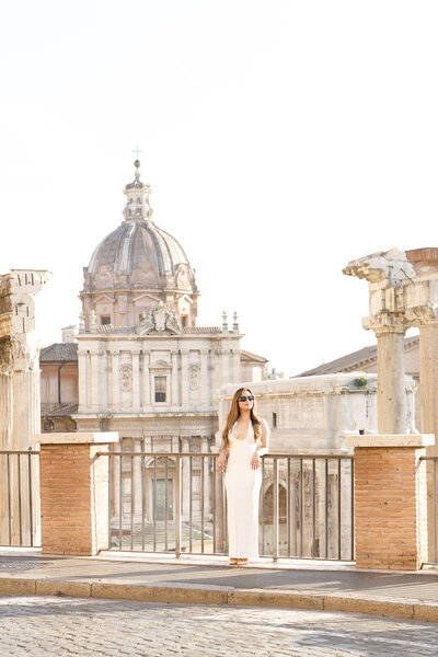 A beautiful girl in a long white dress. She is standing in front of the Roman Forum. Taken by Rome Photographer, Tricia Anne Photography.