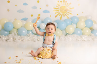 little boy in yellow bow tie and blue suspenders eating cake by Milestone Photographer New Philadelphia