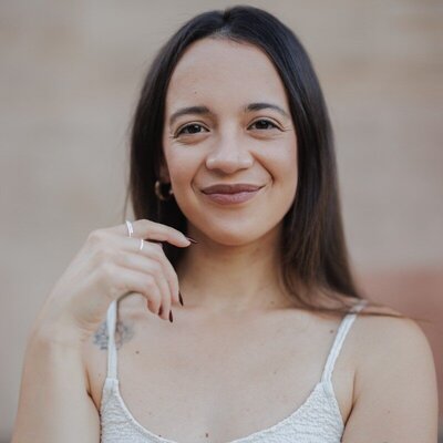 Margherita is smiling. She has dark hair and is wearing a white tank top.