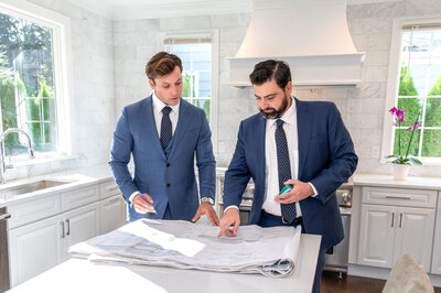 2 men in business suits, standing in a kitchen looking over architectural blueprint plans for a home in Greenwich.