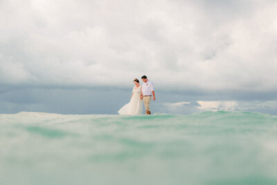 couple walking on beach holding hands with water in foreground