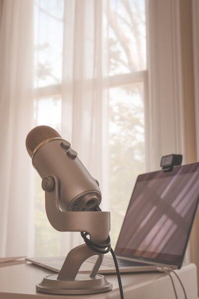 A desk features a microphone alongside a laptop, suggesting an environment for podcasting or virtual meetings.