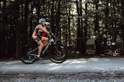 A couple bikes through the woods together during their family vacation