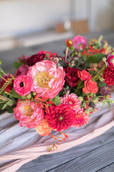 A small red floral centerpiece on top of a light pink cheesecloth. 