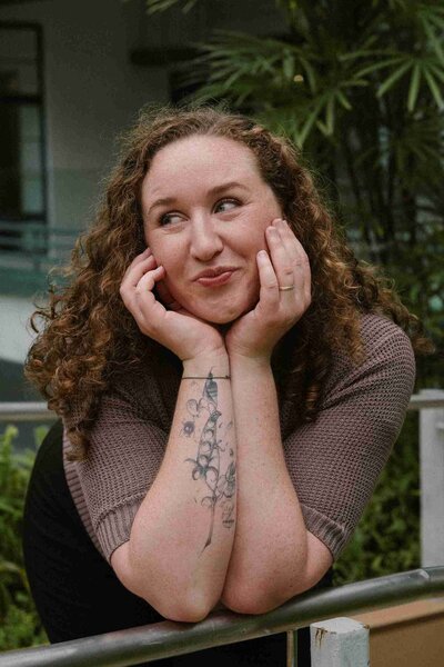 1. A woman with curly hair and tattoos leans on a railing, showcasing her style as a nutritionist.