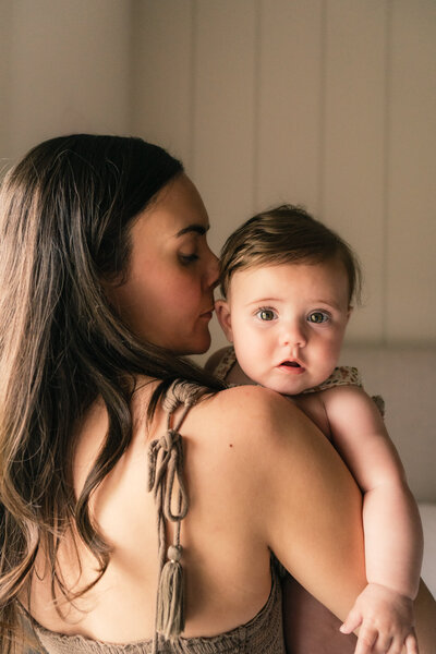 Mum holding little girl and looking down at her over her shoulder.
