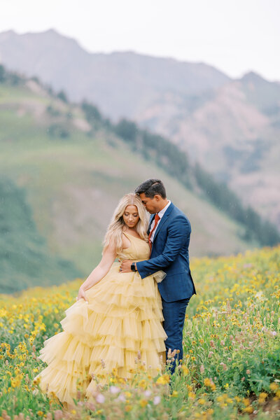 couple in ruffled yellow gown and blue suit stand together in flower field at Albion Basin in Utah