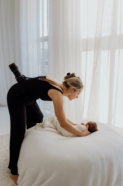 lucy jane, a professional photographer in christchurch laying a newborn baby down on a photography studio prop bed during a newborn photoshoot