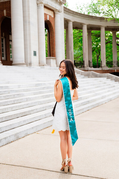 Graduation photo of Zeta Tau Alpha senior standing outside of the Wyatt Center at golden hour with her sorority swag