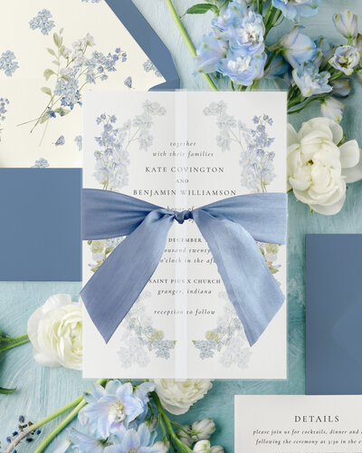 wedding invitation wrapped in vellum and tied with a large blue bow