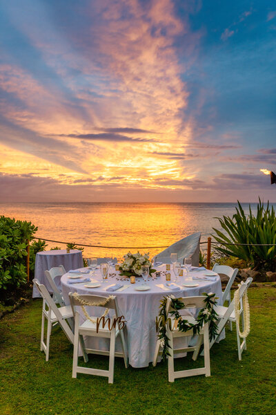 round dinner table set up for dinner with a floral centerpiece overlooking the ocean and a dramatic sunset