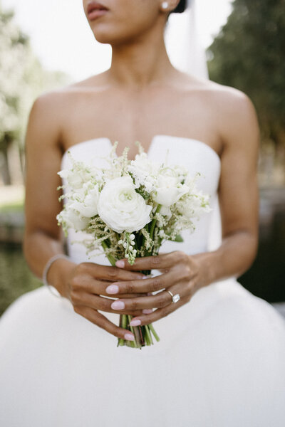 Black bride in white strapless wedding dress holds a bouquet of white flowers