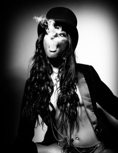 A gorgeous woman in a top hat and tux smoking a cigar in a dramatic old Hollywood glam black & white image.