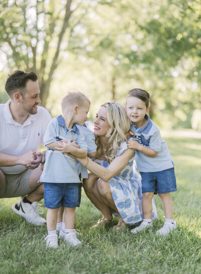 Candid family moment with parents and three young children laughing together during a Kansas City family photography session in a sunlit field.