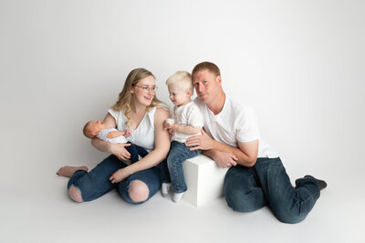 A clean and joyful family portrait featuring a toddler meeting their new sibling, styled in classic white tones for a timeless feel.