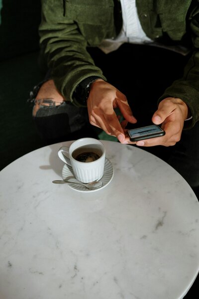 A person enjoying a study break with coffee while checking their phone at a café table