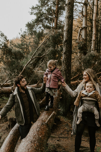 Family walking in woods, girl balancing on tree