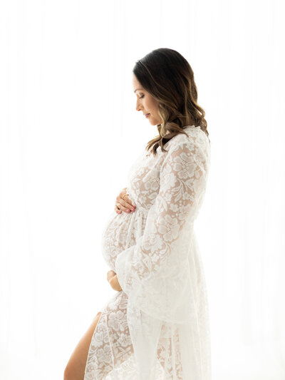 pregnant mother in white lace maternity gown holding baby bump for maternity session