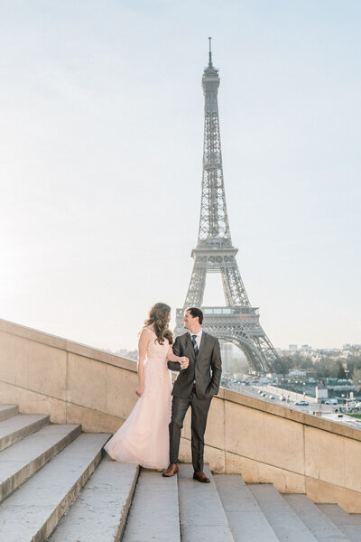 Couple in front of the Eiffel Tower with the man wearing a suit and the woman wearing a pink chiffon dress..