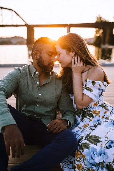 Mixed race engaged couple on a dock by the water at sunset.