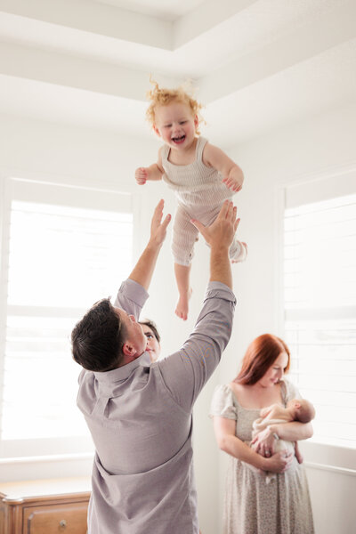 Dad tosses his little girl while mom snuggles her newborn baby brother