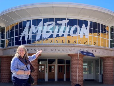 LIsa Rielage points to the Ambition Unleashed sign at the Quinnipiac University Student Center.