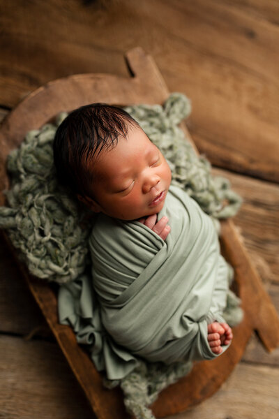 Newborn baby girl wrapped in tiffany blue fabric wearing a matching bow headband during her newborn photography session.