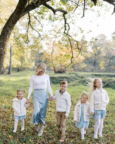 Stephanie Houseal walks hand-in-hand with her four children beneath a golden tree. A family moment behind Moments in Light Photography.