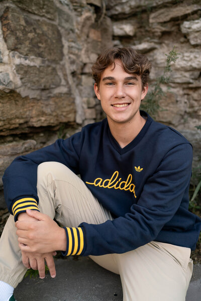 Senior boy in blue Adidas shirt shirts against rock wall.