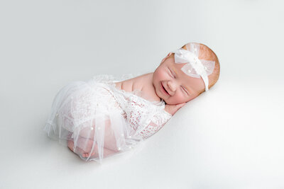 Sweet Newborn Smile in Soft White Outfit on white blanket