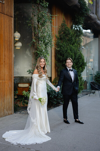 Newly wed couple sat, holding hands and smiling at the camera