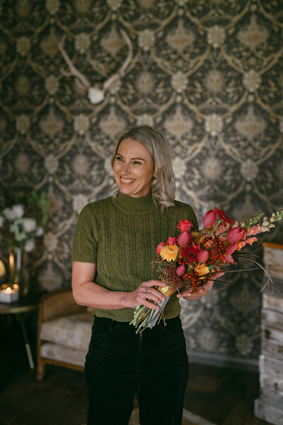 Kirsty the planner smiling and laughing with her head turned away from the camera. She is holding a colourful bouquet of flowers with vibrant pinks, reds and yellows