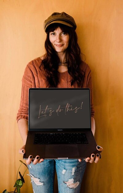 Sara Bowers holding laptop against bright orange wall