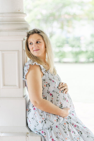 A pregnant mother leans against a white column at the Woodbine Mansion during her maternity photoshoot in Round Rock, TX.
