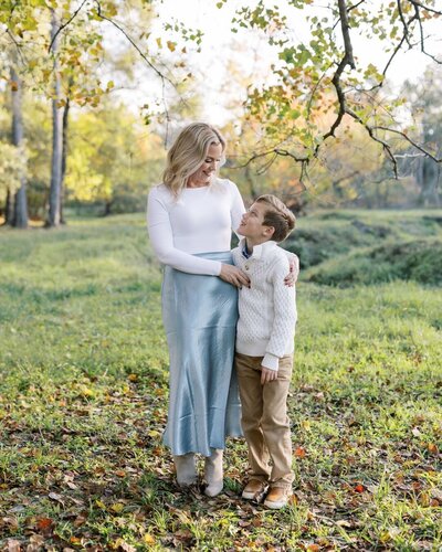 Stephanie Houseal stands in a sunlit field, gently holding her son's hand. A personal moment from the artist behind Moments in Light Photography.