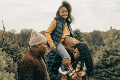 A family dressed in winter clothes smiling while gathered outside surrounded by trees and nature