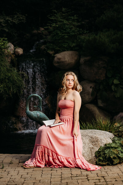 Senior girl reading a book on a rock in front of a waterfall