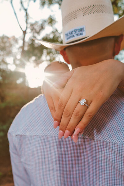 Close-up of brides hand resting on groom's shoulder, showcasing the engagement ring during their proposal at The Rainbow Lounge in Houston, Texas, with soft golden light in the background.