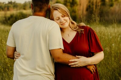 Midwest couple snuggles together holding wife's growing baby bump.