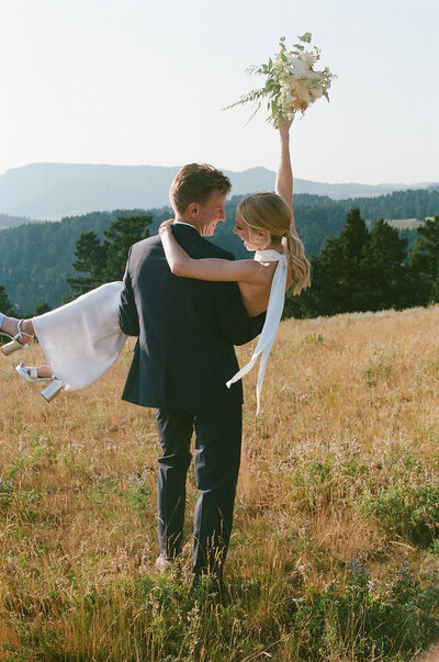 groom holding bride and walking away on mountaintop in bozeman