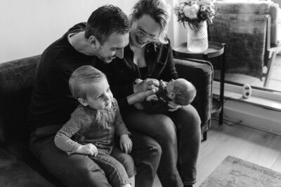 Black and white family portrait with parents smiling at their baby during lifestyle photoshoot