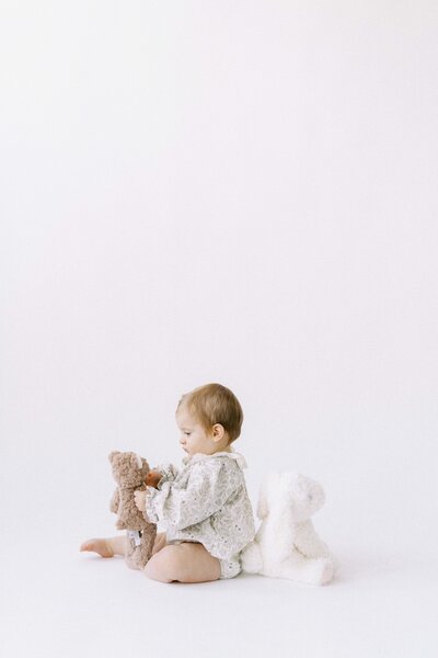 one year old girl sitting with stuffed animals at milestone session