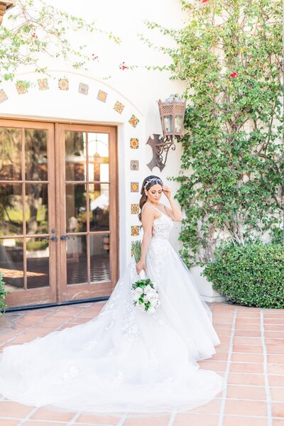 Bride wearing wedding ballgown holding long white rose bouquet in front of the Villa at Hummingbird Nest Ranch Villa.