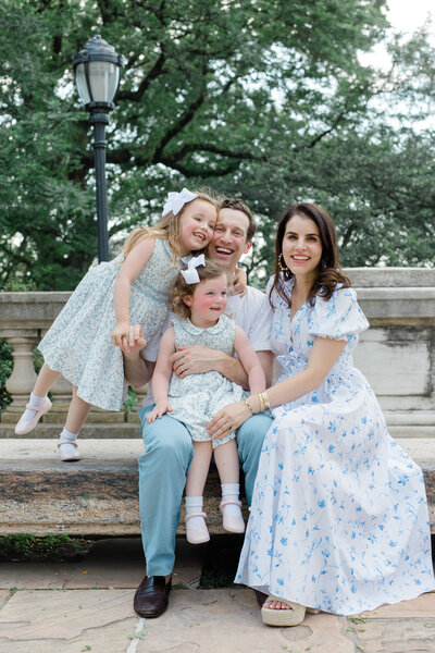 Family of 4 sitting outdoors at a park by NYC family photographer