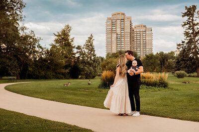 family of three snuggle and kiss in downtown city park in Denver Colorado on a  warm sunny day