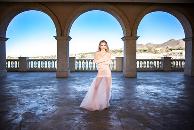 senior girl in a gown framed underneath arches with a beach in las vegas in the background