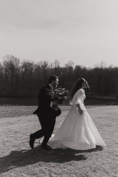 couple with a bouquet running through a field of grass