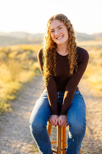 Sitting on a stool, Haylee smiles at the camera. She's slightly leaning forward putting her weight on her hands on the stool.